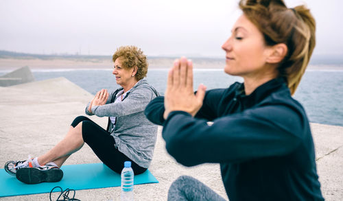 Women doing yoga at beach against sky