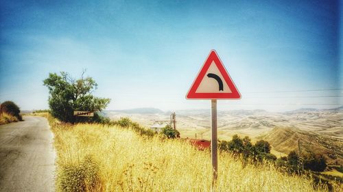 Road sign on landscape against blue sky