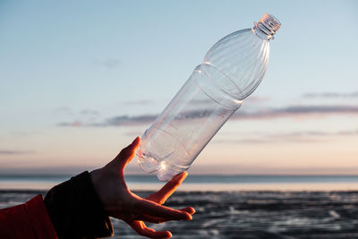 A human hand holds a plastic bottle thrown on the shore. 
