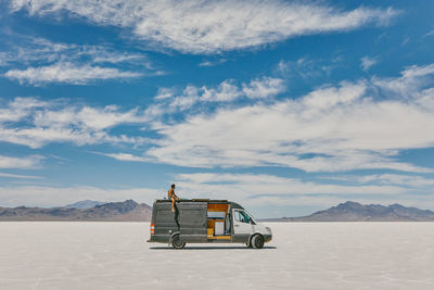 Young man sitting on roof of camper van in bonneville salt flats.