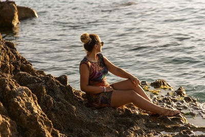 Side view of woman sitting on rock at beach