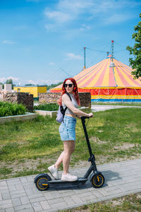 Young bright woman smiles and rides electric scooter in the summer in the city