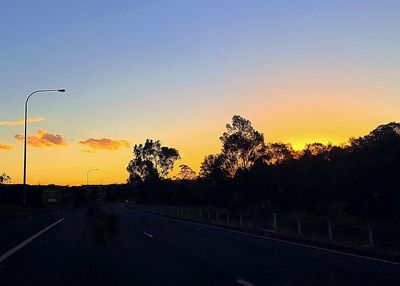 Road by silhouette trees against sky during sunset