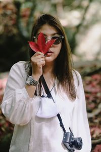 Portrait of beautiful young woman holding red while standing outdoors