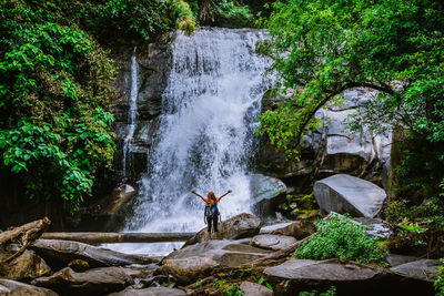 Man standing on rock against waterfall in forest