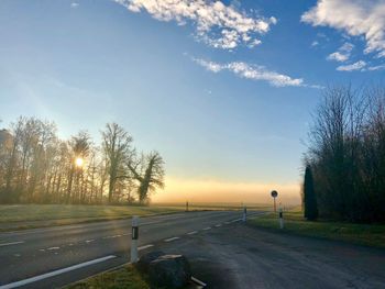 Road by trees against sky during sunset