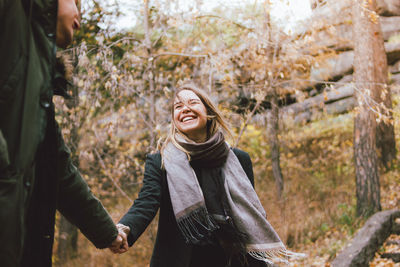 Smiling young woman holding hands while standing against trees