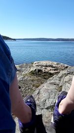 Low section of man sitting on rock by sea against clear sky