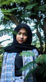 Portrait of young woman standing against plants