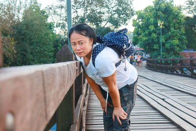 Portrait of woman with backpack standing by railing on footbridge