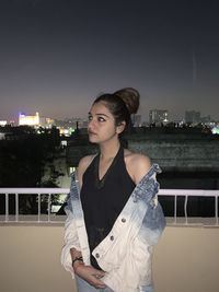 Portrait of beautiful young woman standing against cityscape against sky