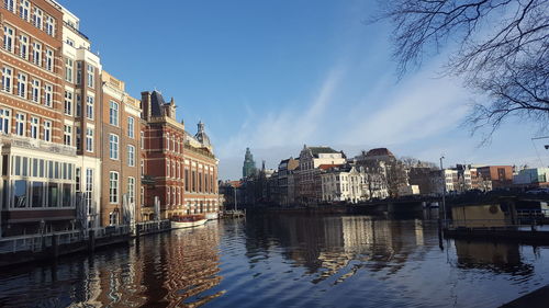 Canal by cityscape against sky