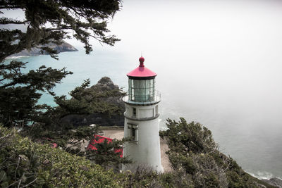Lighthouse by building against sky