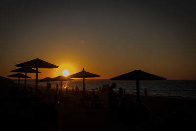 Silhouette people on beach against sky during sunset