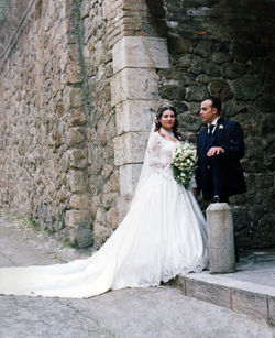 Portrait of bride with groom standing against wall