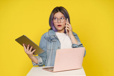 Portrait of young woman using mobile phone against yellow background