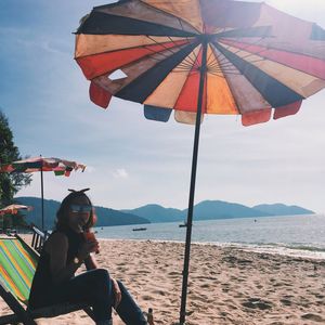 Woman sitting on beach against sky