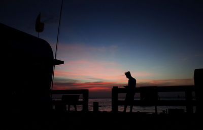 Silhouette man sitting by sea against sky during sunset