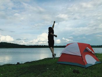 Woman standing on grass by lake against sky