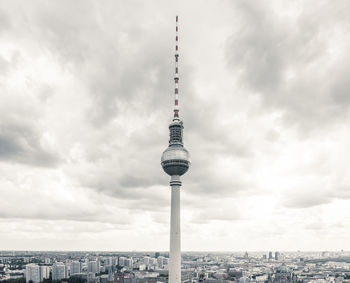 Communications tower in city against cloudy sky