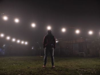 Rear view of man walking on illuminated street at night