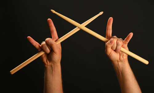 Cropped hands with rock sign holding drumsticks against black background