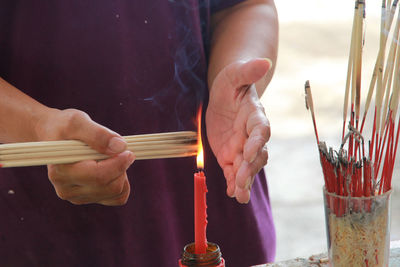 Midsection of man igniting incense on burning candles in temple