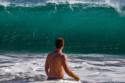 Rear view of shirtless man standing against wave