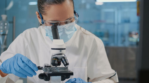 Scientist wearing mask looking through microscope