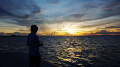 Silhouette man fishing in sea against sunset sky