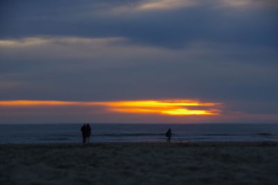 Silhouette people on beach against sky during sunset