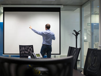 Rear view of businessman standing by projection screen in board room at office