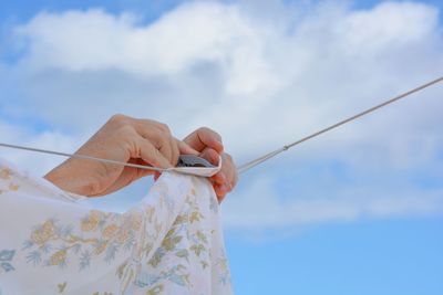 Cropped hands holding clothespin on clothesline against sky