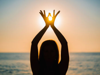 Silhouette woman doing yoga at beach against sky