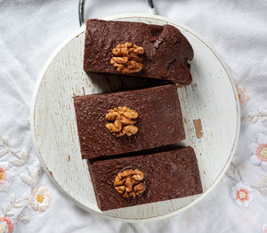 Baked pieces of brownie chocolate cake with nuts on a round wooden board, delicious dessert, t