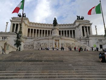 People on steps of building against cloudy sky