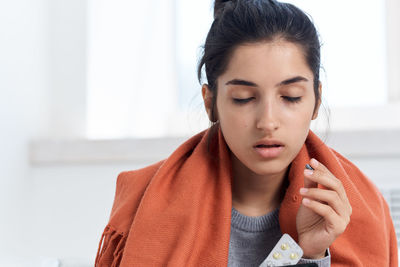 Sick young woman holding medicine wearing blanket