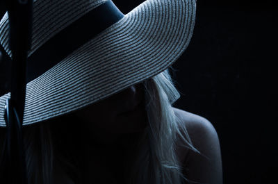 Close-up portrait of woman wearing hat against black background