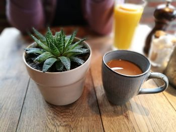 Close-up of coffee by potted cactus on wooden table