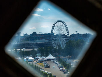 Ferris wheel in city against sky seen through glass window