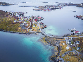 Drone view of residential buildings located on grassy lofoten islands with roads and bridge near calm clear sea in norway