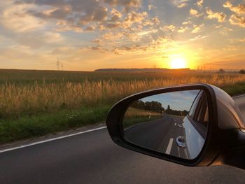 View of road through side-view mirror by agricultural field against cloudy sky