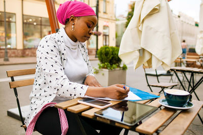 Portrait of young woman using mobile phone while sitting on table