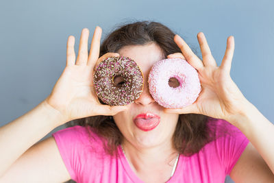 Cheerful woman holding donuts against wall