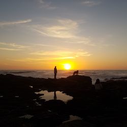 Silhouette people standing on beach against sky during sunset