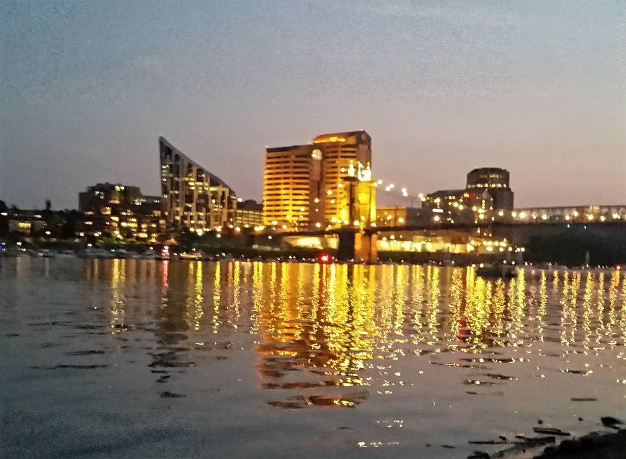 ILLUMINATED BUILDINGS BY RIVER AGAINST SKY