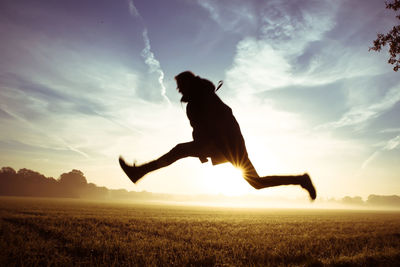 Silhouette man jumping above grassy field against sky