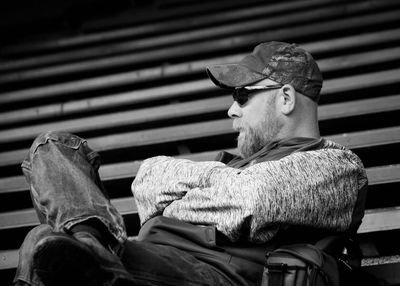 Man with arms crossed sitting on bleachers at football stadium