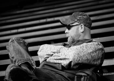 Man with arms crossed sitting on bleachers at football stadium