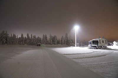 Snow covered road by trees against sky at night during winter